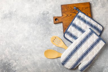 Ahşap mutfak aletleri, kesim tahtası, tutacağı ve eldiven masanın üstünde. Mutfak eldiveni ve koruyucu fırın eldivenleri masanın üstünde. Mutfak eşyaları. Mutfak aksesuarları. Yakın çekim. Üst manzara..