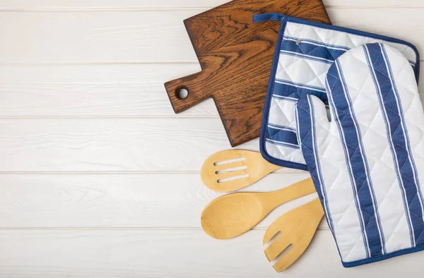 Ahşap mutfak aletleri, kesim tahtası, tutacağı ve eldiven masanın üstünde. Mutfak eldiveni ve koruyucu fırın eldivenleri masanın üstünde. Mutfak eşyaları. Mutfak aksesuarları. Yakın çekim. Üst manzara..