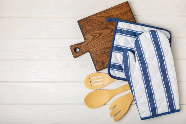 Ahşap mutfak aletleri, kesim tahtası, tutacağı ve eldiven masanın üstünde. Mutfak eldiveni ve koruyucu fırın eldivenleri masanın üstünde. Mutfak eşyaları. Mutfak aksesuarları. Yakın çekim. Üst manzara..