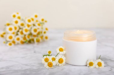 Yüz, vücut ve eller için açık bir nemlendirici krem kavanozu ve hafif bir arka planda papatya çiçeği. Bitki dermatolojik kozmetik hijyen kremi. Doğal kozmetik ürünü. Güzellik konsepti. ÇEVİRİ