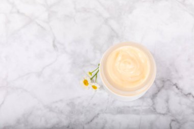 Yüz, vücut ve eller için açık bir nemlendirici krem kavanozu ve hafif bir arka planda papatya çiçeği. Bitki dermatolojik kozmetik hijyen kremi. Doğal kozmetik ürünü. Güzellik konsepti. ÇEVİRİ