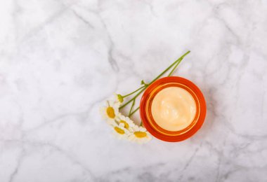 Yüz, vücut ve eller için açık bir nemlendirici krem kavanozu ve hafif bir arka planda papatya çiçeği. Bitki dermatolojik kozmetik hijyen kremi. Doğal kozmetik ürünü. Güzellik konsepti. ÇEVİRİ