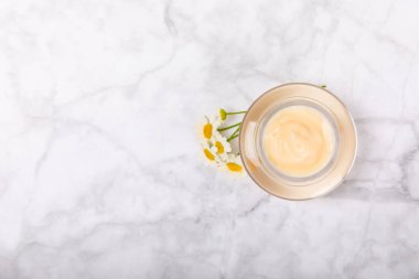 Yüz, vücut ve eller için açık bir nemlendirici krem kavanozu ve hafif bir arka planda papatya çiçeği. Bitki dermatolojik kozmetik hijyen kremi. Doğal kozmetik ürünü. Güzellik konsepti. ÇEVİRİ