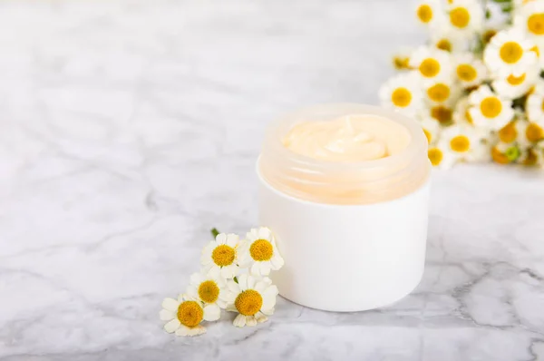 Open jar of moisturizing cream for face, body and hands with a chamomile flower on a light background. Herbal dermatological cosmetic hygiene cream. Natural cosmetic product. Beauty concept. MOCKUP