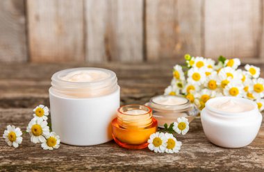 Ağaç zemin üzerinde papatya çiçeği olan yüz, vücut ve eller için açık bir krem kavanozu. Bitki dermatolojik kozmetik hijyen kremi. Doğal kozmetik ürünü. Güzellik konsepti. Kozmetik tüpü..