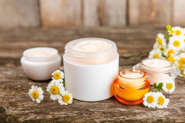 Ağaç zemin üzerinde papatya çiçeği olan yüz, vücut ve eller için açık bir krem kavanozu. Bitki dermatolojik kozmetik hijyen kremi. Doğal kozmetik ürünü. Güzellik konsepti. Kozmetik tüpü..