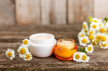 Ağaç zemin üzerinde papatya çiçeği olan yüz, vücut ve eller için açık bir krem kavanozu. Bitki dermatolojik kozmetik hijyen kremi. Doğal kozmetik ürünü. Güzellik konsepti. Kozmetik tüpü..