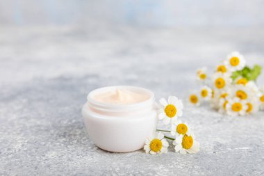 Mavi arka planda papatya çiçeği olan yüz, vücut ve eller için açık bir krem kavanozu. Bitki dermatolojik kozmetik hijyen kremi. Doğal kozmetik ürünü. Güzellik konsepti. Kozmetik tüp. Metin için MOCKUP.s..