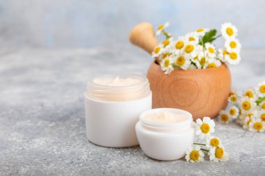Mavi arka planda papatya çiçeği olan yüz, vücut ve eller için açık bir krem kavanozu. Bitki dermatolojik kozmetik hijyen kremi. Doğal kozmetik ürünü. Güzellik konsepti. Kozmetik tüp. Metin için MOCKUP.s..
