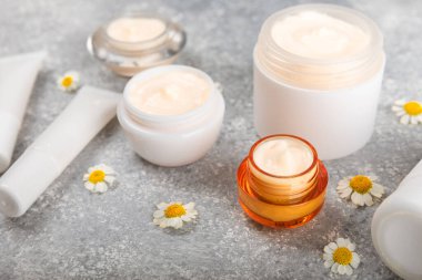 Mavi arka planda papatya çiçeği olan yüz, vücut ve eller için açık bir krem kavanozu. Bitki dermatolojik kozmetik hijyen kremi. Doğal kozmetik ürünü. Güzellik konsepti. Kozmetik tüp. Metin için MOCKUP.s..