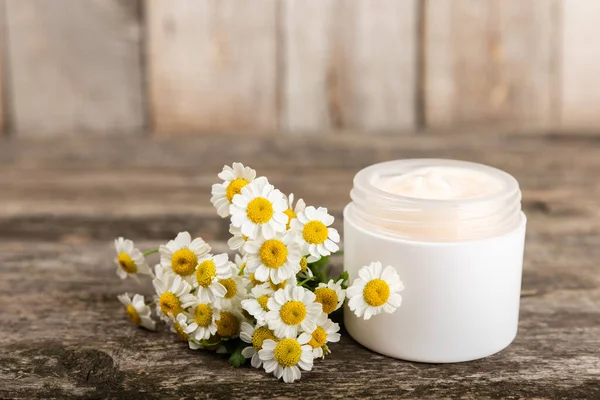 Open jar of cream for face, body and hands with chamomile flower on a wooden background. Herbal dermatological cosmetic hygiene cream. Natural cosmetic product. Beauty concept. Cosmetic tube.MOCKUP.