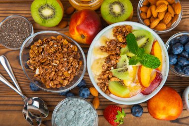 Bir kase granola yoğurt ve dokuma masasında taze böğürtlen. Yoğurt böğürtlen, acai kasesi, spirulina kasesi. Sağlıklı yemek, dengeli kahvaltı. Çilek, yabanmersini, kivi, şeftali, badem ve chia.. 
