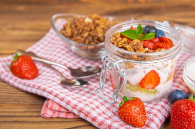 Bir kase granola yoğurt ve dokuma masasında taze böğürtlen. Yoğurt böğürtlen, acai kasesi, spirulina kasesi. Sağlıklı yemek, dengeli kahvaltı. Çilek, yabanmersini, kivi, şeftali, badem ve chia.. 