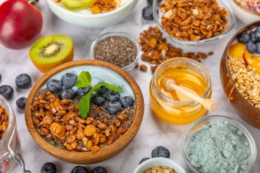 Bir kase granola yoğurt ve dokuma masasında taze böğürtlen. Yoğurt böğürtlen, acai kasesi, spirulina kasesi. Sağlıklı yemek, dengeli kahvaltı. Çilek, yabanmersini, kivi, şeftali, badem ve chia.. 