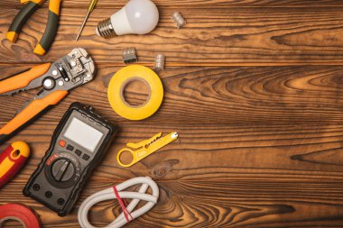 Tahta arka planda kopyalanmış elektrik ekipmanları. Üst görünüm. Elektrik aleti seti. Çoklu metre, test cihazı, tornavida, kesiciler, koli bandı, lamba, mezura, mezura ve kablo.