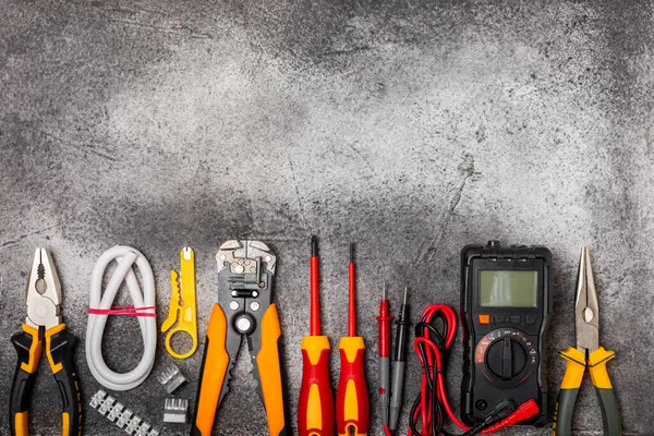 Siyah desenli arka plan üzerindeki elektrikli ekipman. Üst görünüm. Elektrik aracı seti. Çoklu metre, testçi, tornavida, kesiciler, koli bandı, lamba, mezura, mezura ve kablo.
