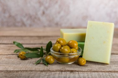 Kahverengi desenli ahşap üzerine zeytinyağı özlü doğal sabun. Yeşil, besleyici sabun ve zeytin çileği parçaları. Vücut bakımı ve spa konsepti. Metin için yer. Boşluğu kopyala. Düz konum