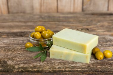 Kahverengi desenli ahşap üzerine zeytinyağı özlü doğal sabun. Yeşil, besleyici sabun ve zeytin çileği parçaları. Vücut bakımı ve spa konsepti. Metin için yer. Boşluğu kopyala. Düz konum