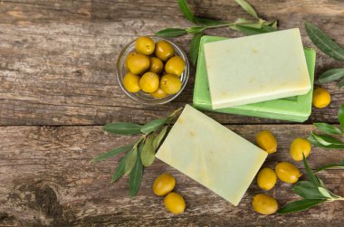 Kahverengi desenli ahşap üzerine zeytinyağı özlü doğal sabun. Yeşil, besleyici sabun ve zeytin çileği parçaları. Vücut bakımı ve spa konsepti. Metin için yer. Boşluğu kopyala. Düz konum