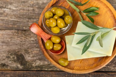 Kahverengi desenli ahşap üzerine zeytinyağı özlü doğal sabun. Yeşil, besleyici sabun ve zeytin çileği parçaları. Vücut bakımı ve spa konsepti. Metin için yer. Boşluğu kopyala. Düz konum