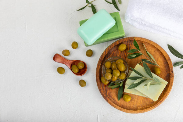 Натуральный кусок мыла с экстрактом оливкового масла на белом текстурированном дереве. Кусочки зеленого питательного мыла и оливковых ягод. Концепция ухода за телом и спа. Место для текстуры.