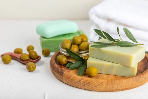 Natural bar of soap with olive oil extract on white textured wood. Pieces of green nourishing soap and olive berries. Body care and spa concept. Place for text.Copy space.Flat lay