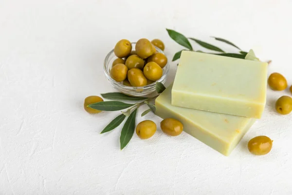 Natural bar of soap with olive oil extract on white textured wood. Pieces of green nourishing soap and olive berries. Body care and spa concept. Place for text.Copy space.Flat lay
