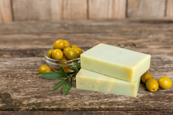 Natural bar of soap with olive oil extract on brown textured wood. Pieces of green nourishing soap and olive berries. Body care and spa concept. Place for text.Copy space.Flat lay