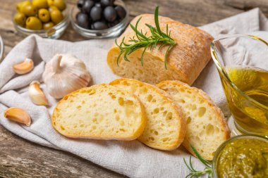 Ciabatta ve zeytin. Otlu taze İtalyan ciabatta ekmeği, zeytinyağı, parmesan ve pesto sosu, ahşap arka planda zeytin, üst manzara, kopyalama alanı. Mesaj için yer. Boşluğu kopyala.