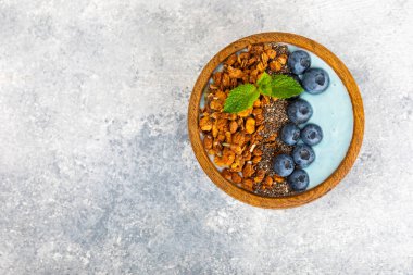 Bir kase granola yoğurt ve dokuma masasında taze böğürtlen. Yoğurt böğürtlen, acai kasesi, spirulina kasesi. Sağlıklı yemek, dengeli kahvaltı. Çilek, yabanmersini, kivi, şeftali, badem ve chia..