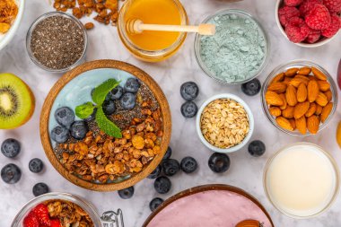 Bir kase granola yoğurt ve dokuma masasında taze böğürtlen. Yoğurt böğürtlen, acai kasesi, spirulina kasesi. Sağlıklı yemek, dengeli kahvaltı. Çilek, yabanmersini, kivi, şeftali, badem ve chia..