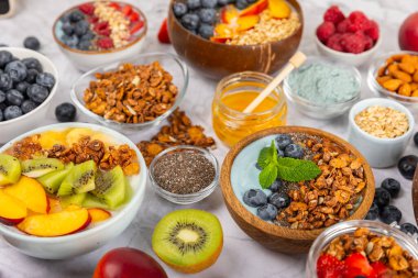 Bir kase granola yoğurt ve dokuma masasında taze böğürtlen. Yoğurt böğürtlen, acai kasesi, spirulina kasesi. Sağlıklı yemek, dengeli kahvaltı. Çilek, yabanmersini, kivi, şeftali, badem ve chia..