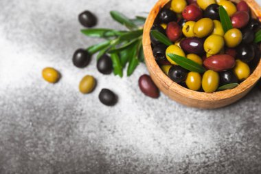 Mermer zemin üzerinde yeşil, kırmızı ve siyah zeytin seti. Kâselerde çeşitli zeytin ve taze zeytin yaprakları. Vejetaryen. Zeytin meyveleri. Mesaj için yer. Boşluğu kopyala.