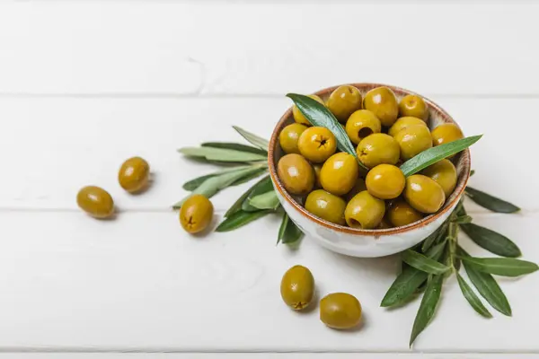 Greens olives on a white wooden background. Various types of olives in bowls and olive oil with fresh olive leaves. Copy space. Place for text. Mediterranean food. Vegan.