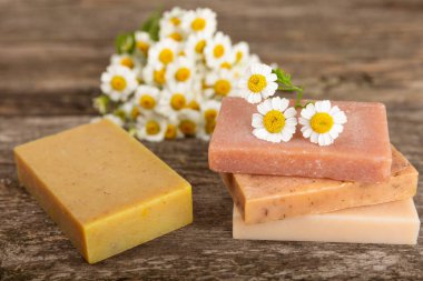 Ahşap bir masada papatya çiçekli doğal ev yapımı sabun. Doğal bitkisel yağlarla nemlendirici sabun yakın plan. Spa ve güzellik konsepti. Mesaj için yer. Uzayı kopyala. Fletley