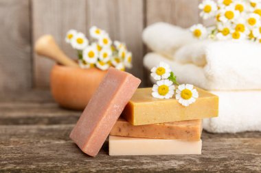 Ahşap bir masada papatya çiçekli doğal ev yapımı sabun. Doğal bitkisel yağlarla nemlendirici sabun yakın plan. Spa ve güzellik konsepti. Mesaj için yer. Uzayı kopyala. Fletley