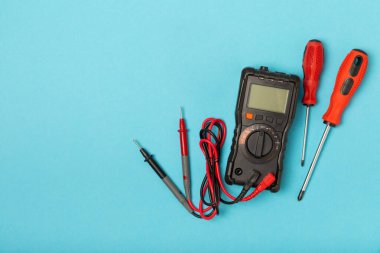 Mavi arka planda elektrikli aletler. Multimetre, inşaat bandı, elektrik bandı, tornavida, pense, otomatik yalıtım striptizcisi, soket ve LED lamba..