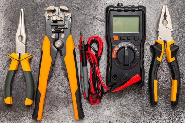 Electrician tools on black marble background.Multimeter,construction tape,electrical tape, screwdrivers,pliers,an automatic insulation stripper, socket and LED lamp.Flatley.electrician concept.