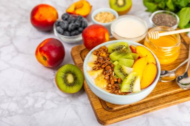 Bir kase granola yoğurt ve dokuma masasında taze böğürtlen. Yoğurt böğürtlen, acai kasesi, spirulina kasesi. Sağlıklı yemek, dengeli kahvaltı. Çilek, yabanmersini, kivi, şeftali, badem ve chia..