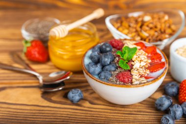 Bir kase granola yoğurt ve dokuma masasında taze böğürtlen. Yoğurt böğürtlen, acai kasesi, spirulina kasesi. Sağlıklı yemek, dengeli kahvaltı. Çilek, yabanmersini, kivi, şeftali, badem ve chia..