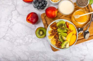 Bir kase granola yoğurt ve dokuma masasında taze böğürtlen. Yoğurt böğürtlen, acai kasesi, spirulina kasesi. Sağlıklı yemek, dengeli kahvaltı. Çilek, yabanmersini, kivi, şeftali, badem ve chia..