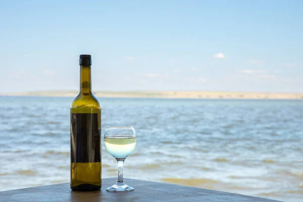 A bottle of white exquisite wine and a glass against the backdrop of a mountain lake.