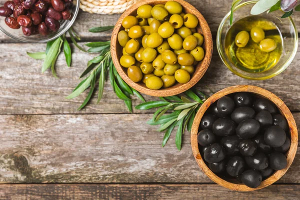 Set of black and green olives on a white wooden background. Various types of olives in wooden bowls and fresh olive leaves. Copy space. Place for text. flat lei. Delicatessen.
