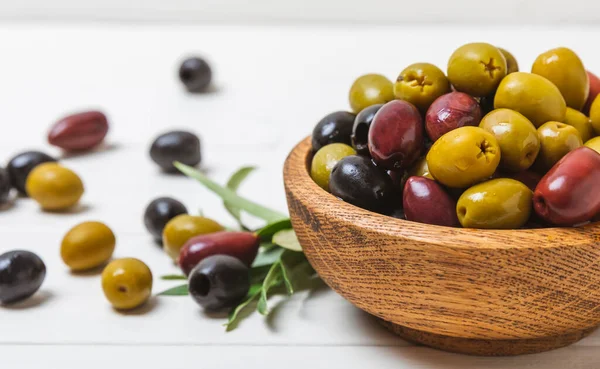 Set of green, red and black olives on a white wooden background. Various types of olives in wooden bowls and fresh olive leaves. Copy space. Place for text. flat lei. Delicatessen.