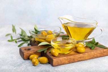 Cam kaselerde zeytinyağı, soslu kayıklar ve dokulu mutfak masasında şişe. Zeytin dallı ve meyveli yağ şişesi. Mesaj için yer. kopyalama alanı. Yemek yağı ve salata sosu. Yakın plan.
