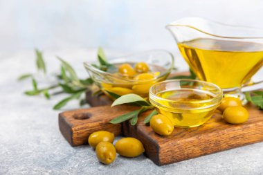 Cam kaselerde zeytinyağı, soslu kayıklar ve dokulu mutfak masasında şişe. Zeytin dallı ve meyveli yağ şişesi. Mesaj için yer. kopyalama alanı. Yemek yağı ve salata sosu. Yakın plan.