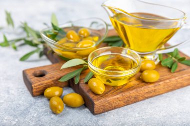 Cam kaselerde zeytinyağı, soslu kayıklar ve dokulu mutfak masasında şişe. Zeytin dallı ve meyveli yağ şişesi. Mesaj için yer. kopyalama alanı. Yemek yağı ve salata sosu. Yakın plan.