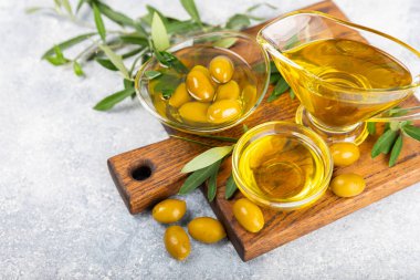 Cam kaselerde zeytinyağı, soslu kayıklar ve dokulu mutfak masasında şişe. Zeytin dallı ve meyveli yağ şişesi. Mesaj için yer. kopyalama alanı. Yemek yağı ve salata sosu. Yakın plan.