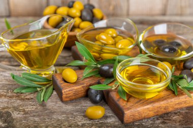 Cam kaselerde zeytinyağı, soslu kayıklar ve dokulu mutfak masasında şişe. Zeytin dallı ve meyveli yağ şişesi. Mesaj için yer. kopyalama alanı. Yemek yağı ve salata sosu. Yakın plan.