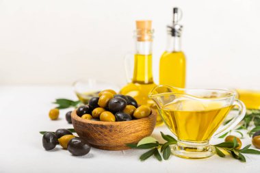 Cam kaselerde zeytinyağı, soslu kayıklar ve dokulu mutfak masasında şişe. Zeytin dallı ve meyveli yağ şişesi. Mesaj için yer. kopyalama alanı. Yemek yağı ve salata sosu. Yakın plan.